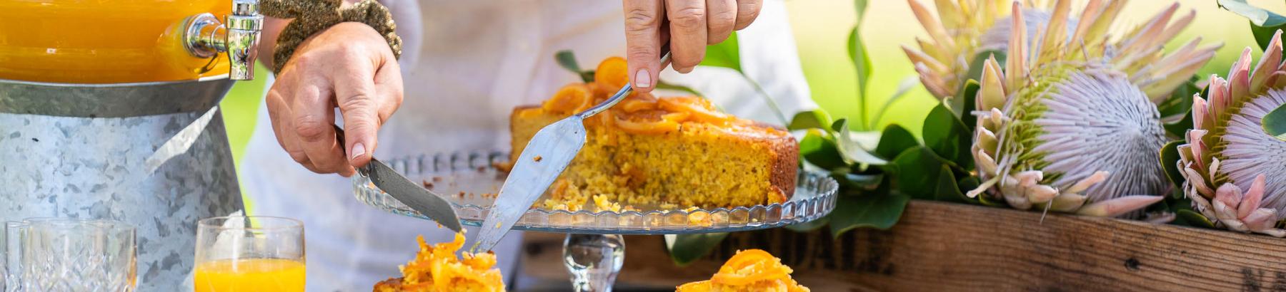 Woman slicing orange and poppyseed cake on rustic picnic bench in Narrandera, NSW
